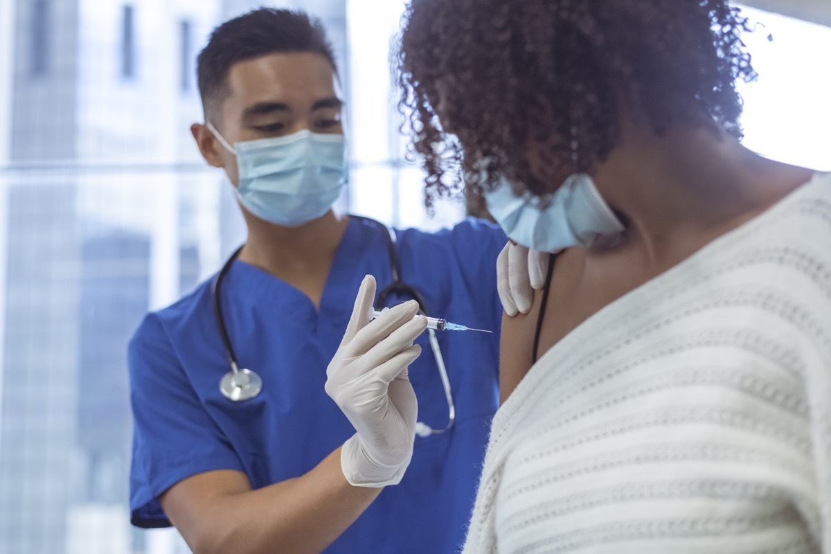 Shot of a male nurse wearing blue medical scrubs, giving vaccine to a woman