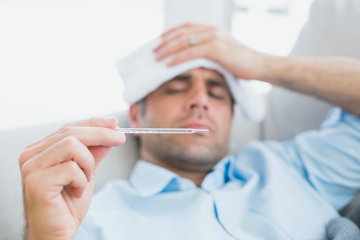 Sick man lying on sofa checking his temperature at home in the living room