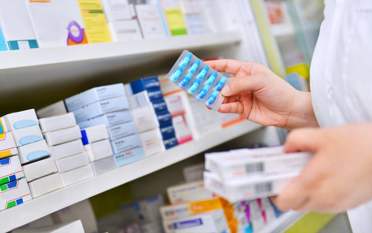 Pharmacist holding medicine box and capsule pack in pharmacy drugstore.