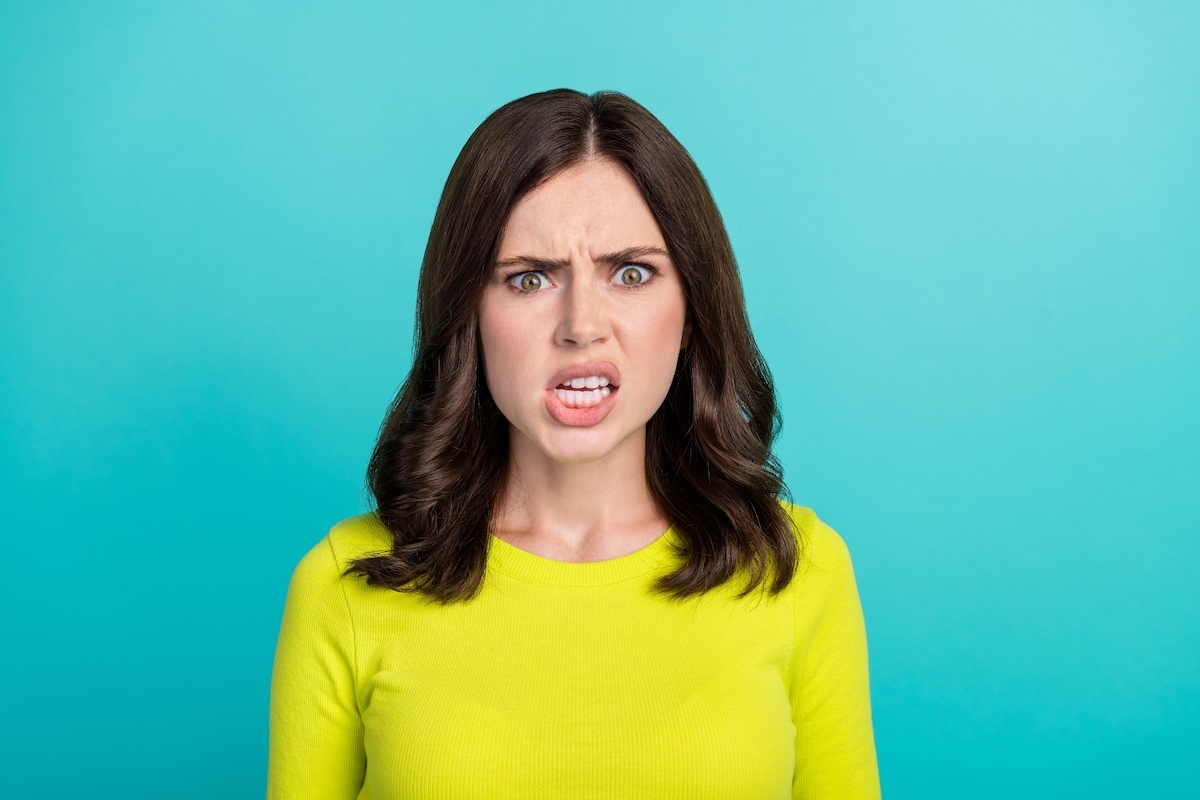 Close up of a frustrated young brunette woman wearing a neon green shirt against a teal background