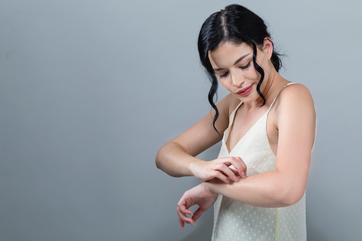 Young woman scratching her itchy arm. Skin problem. on a gray background