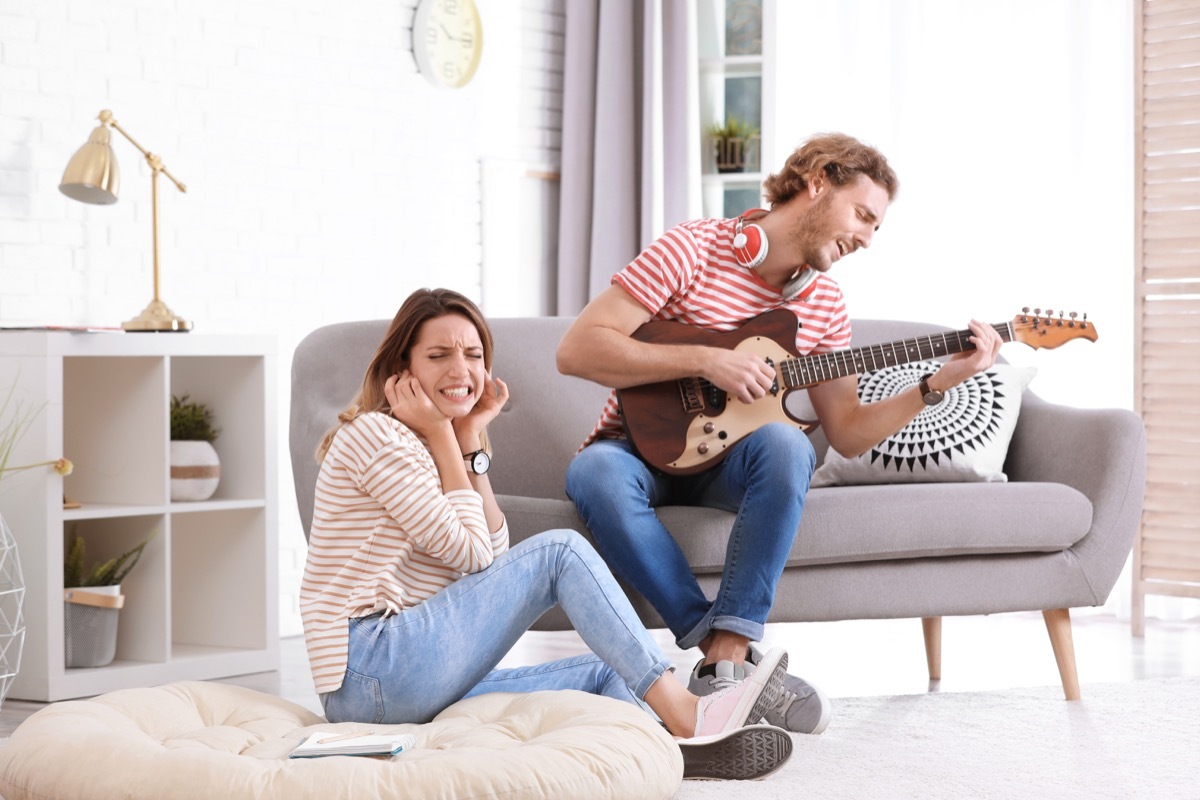 woman closing her ears as man plays guitar