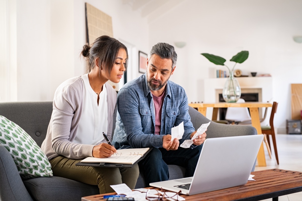 couple sitting at coffee table with notebooks, receipts, and laptop