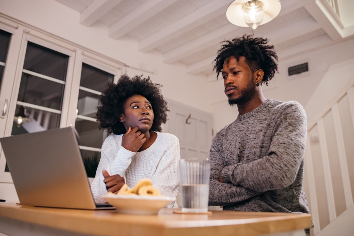 Young couple is looking worried at laptop and talking at home.