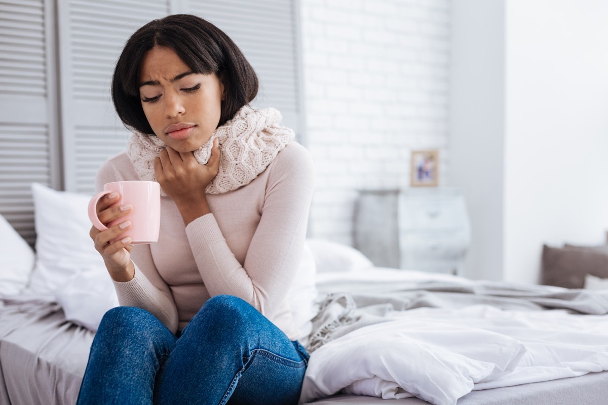 unhappy woman sitting on her bed with sore throat