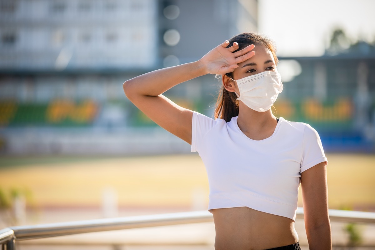 fitness sport woman is resting tired and she wears a mask for protective Dust and pollution on city