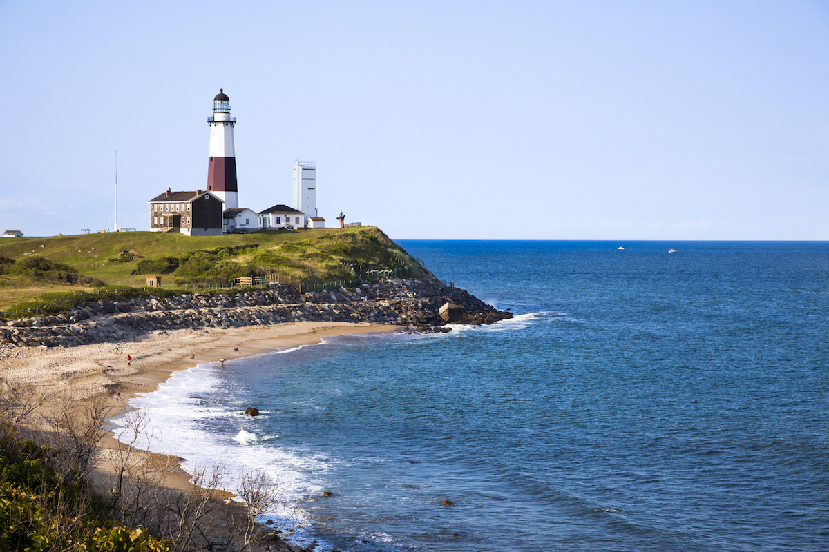 The red and white Montauk Point Lighthouse with the shore and ocean in the foreground.