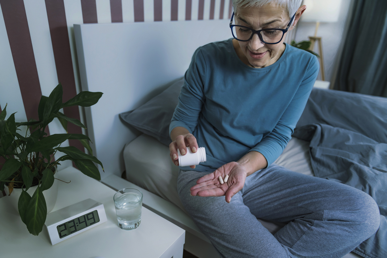 A senior woman sitting in bed prepares to take two supplement pills.