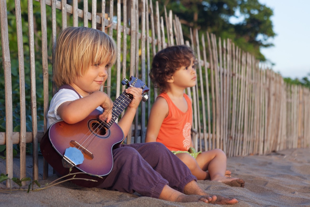 little boys sitting on the beach with a guitar