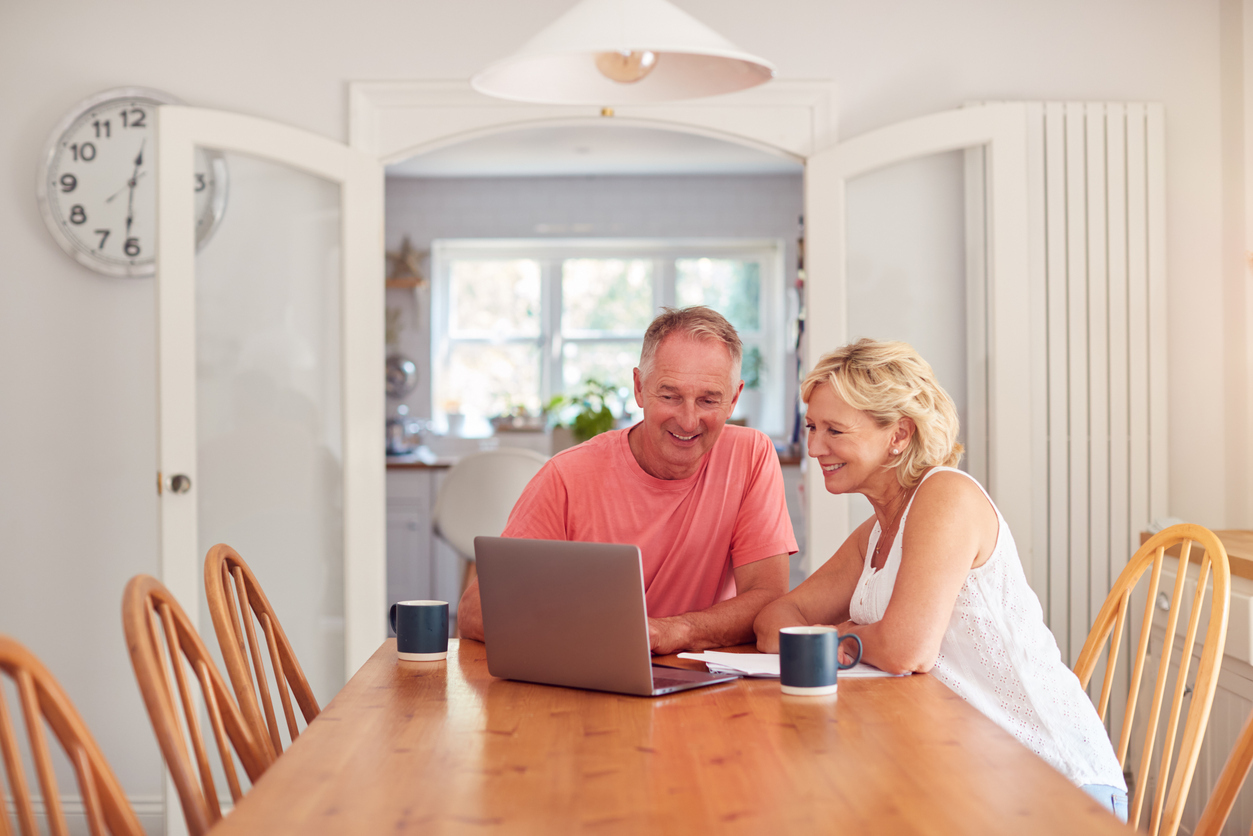 A man and woman couple sitting at the kitchen table looking at a laptop