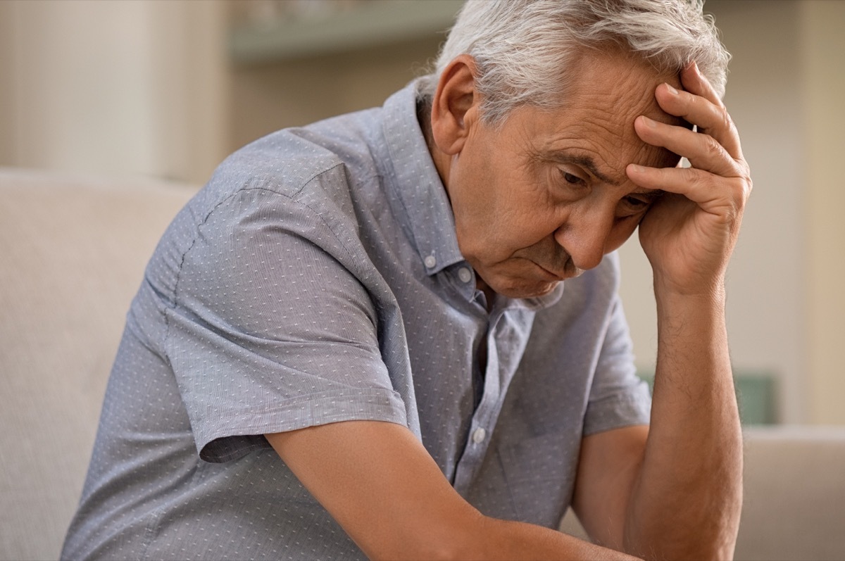 thoughtful senior man sitting on couch. Depressed sad man sitting with hand on head thinking while looking away. Elderly man suffering from alzheimer.