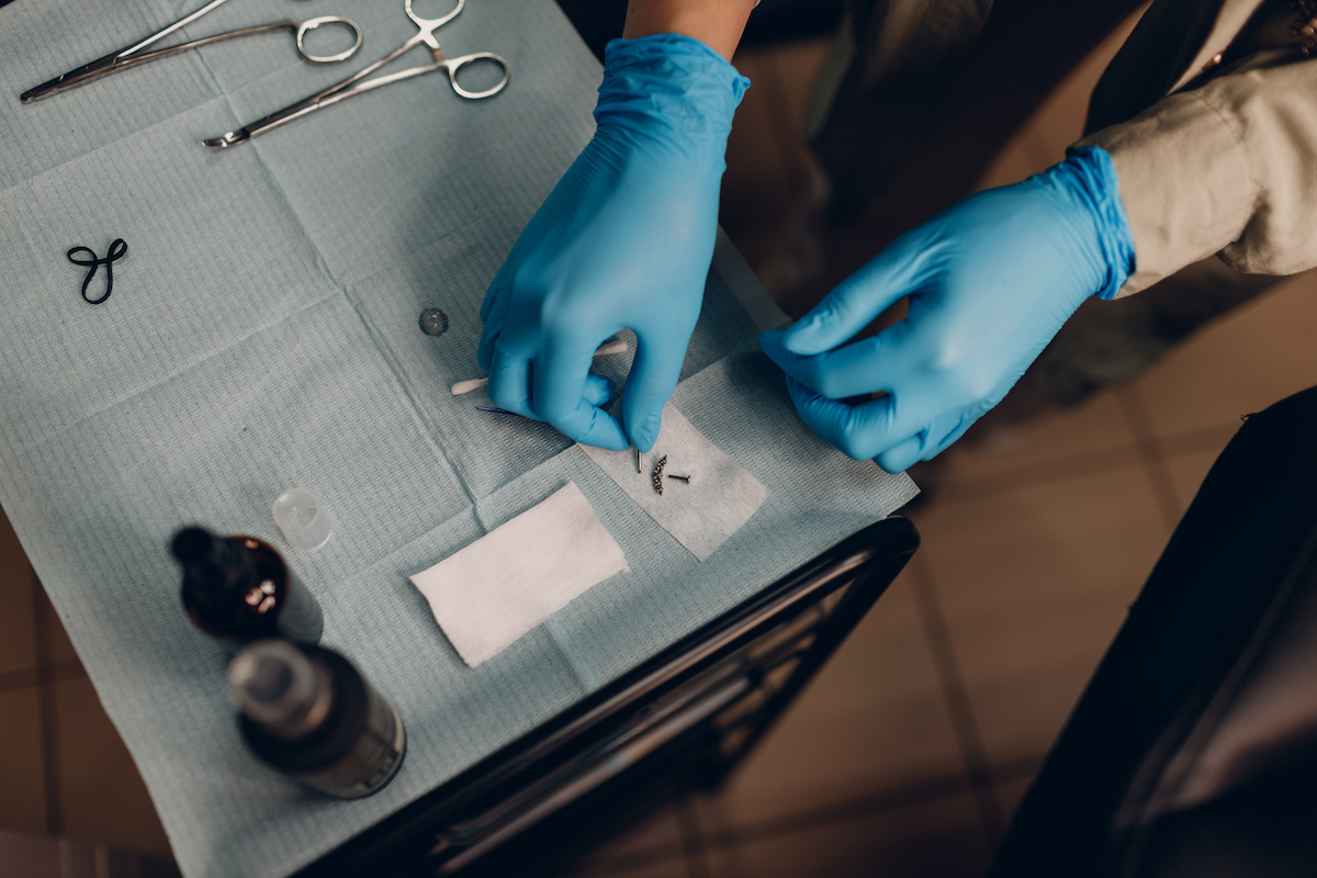 Close up of hands in blue gloves about to do a piercing at beauty studio salon