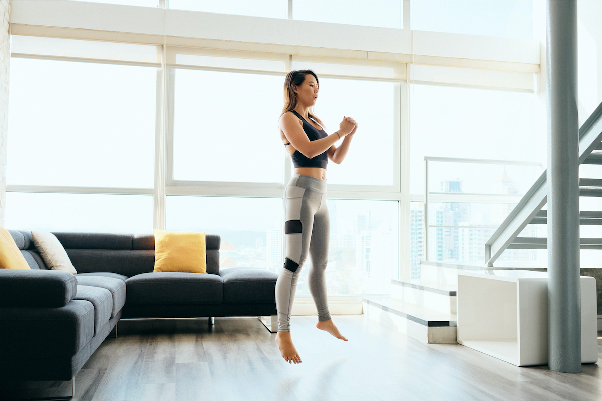 Fit young Pacific Islander woman training at home. Beautiful female athlete working out for wellbeing in domestic gym, training legs muscles with squats and jumps.