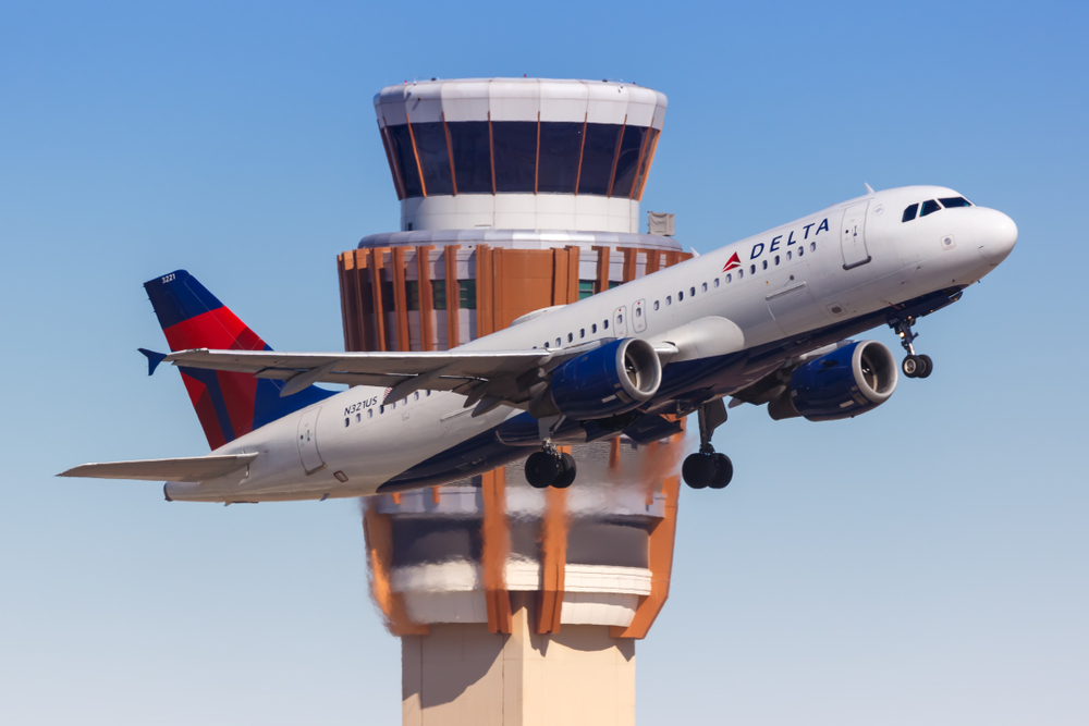 A Delta plane taking off with an air traffic control tower in the background