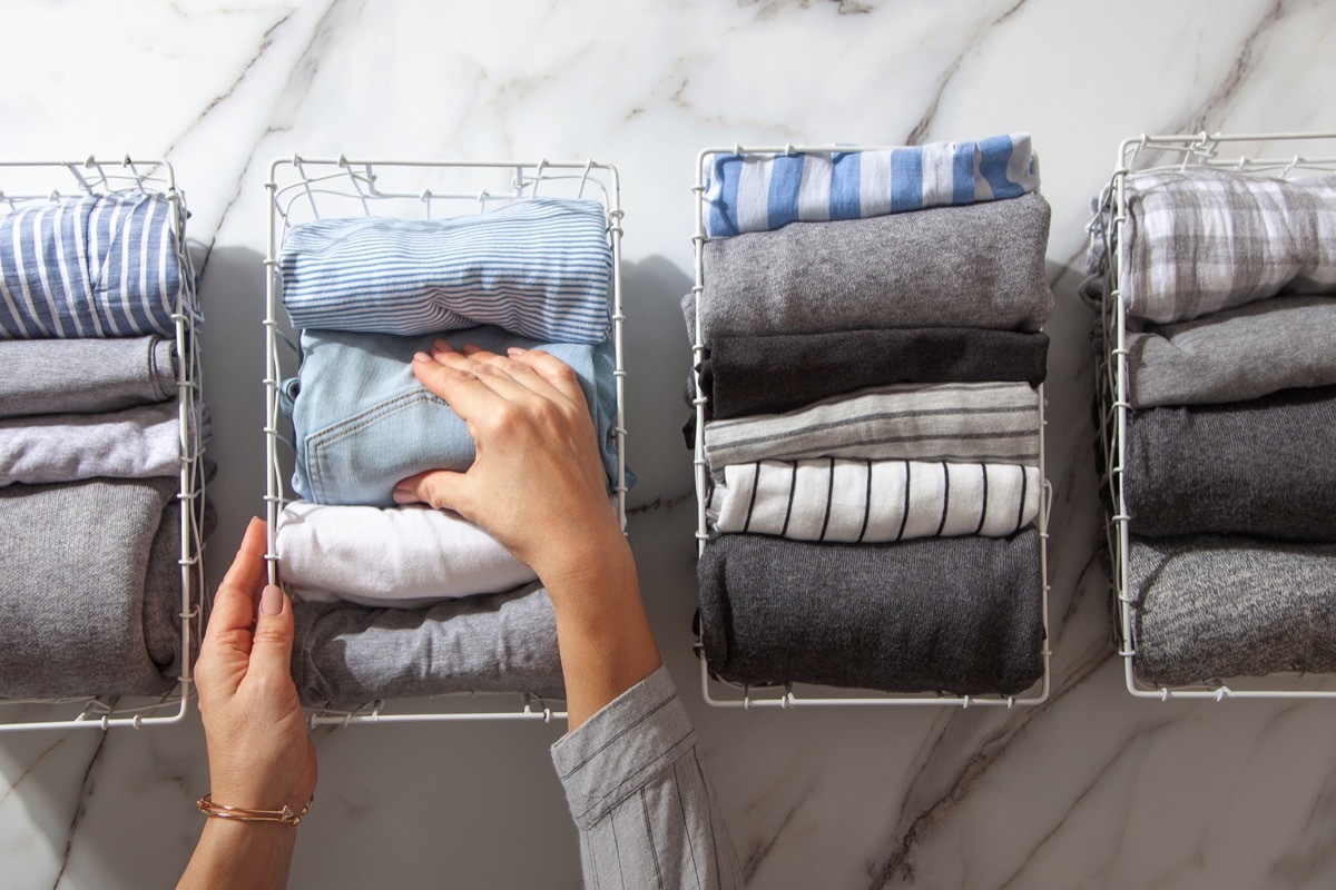 Neatly folded clothes and pyjamas in the metal mesh organizer basket on white marble table. Marie Kondo style of garments declutter and sorting concept. Housewife using Konmari method of tidying up.