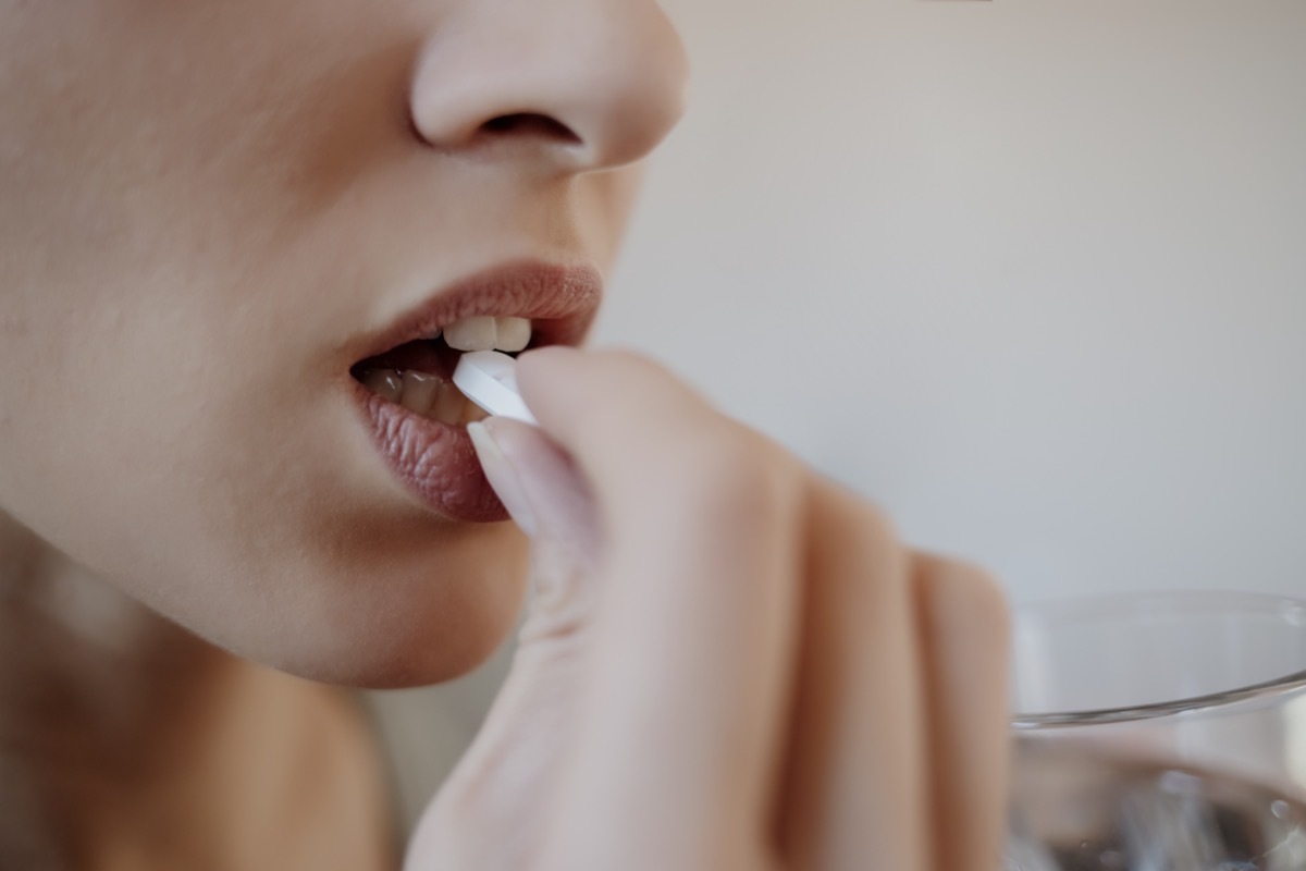 Woman taking tablet with glass of fresh water.