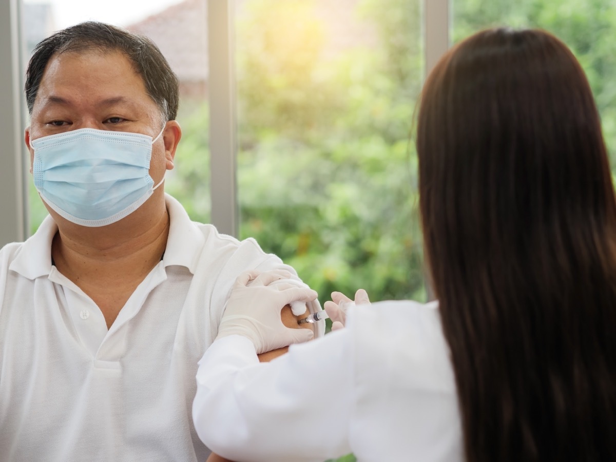 A female doctor wearing gloves and using a syringe with cotton to vaccinate a male patient, covid-19 or coronavirus vaccine.