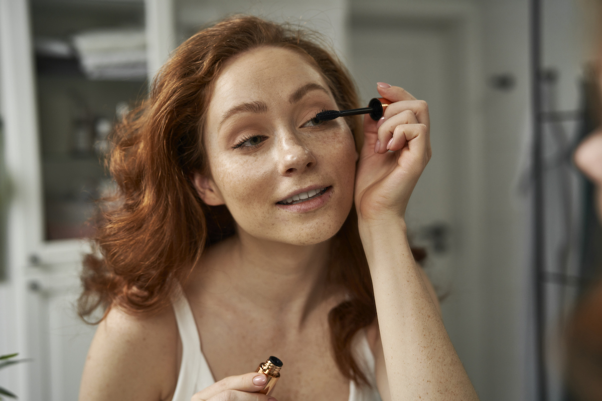 Redhead woman applying mascara in her bathroom mirror