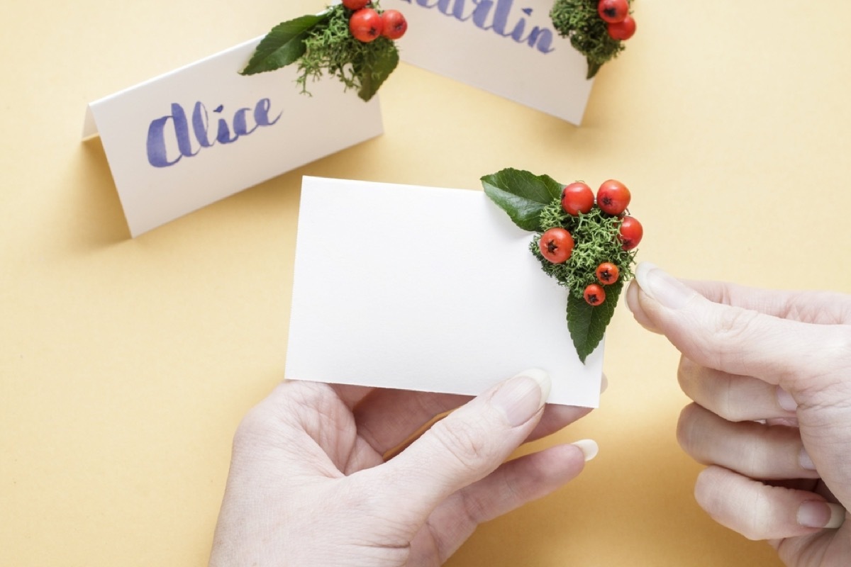 woman holding white place card and attaching holly berries in corner