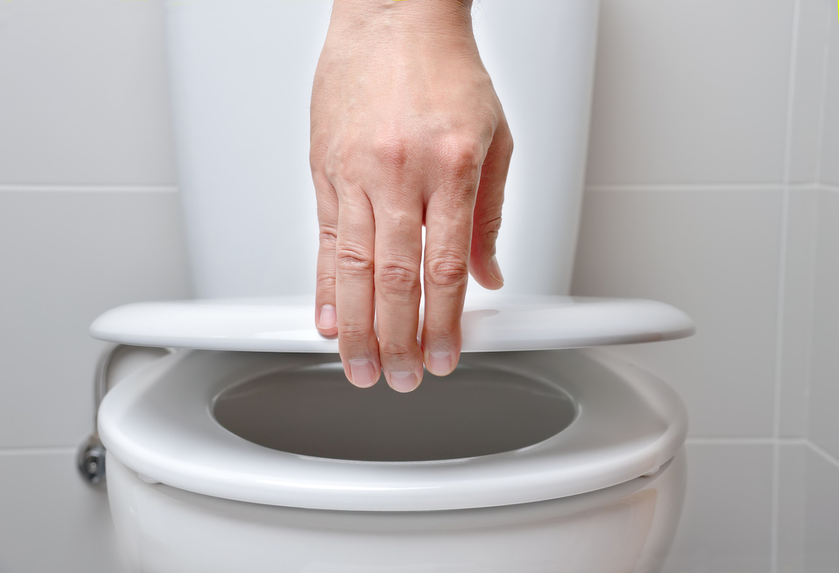 hand of a man closing the lid of a toilet