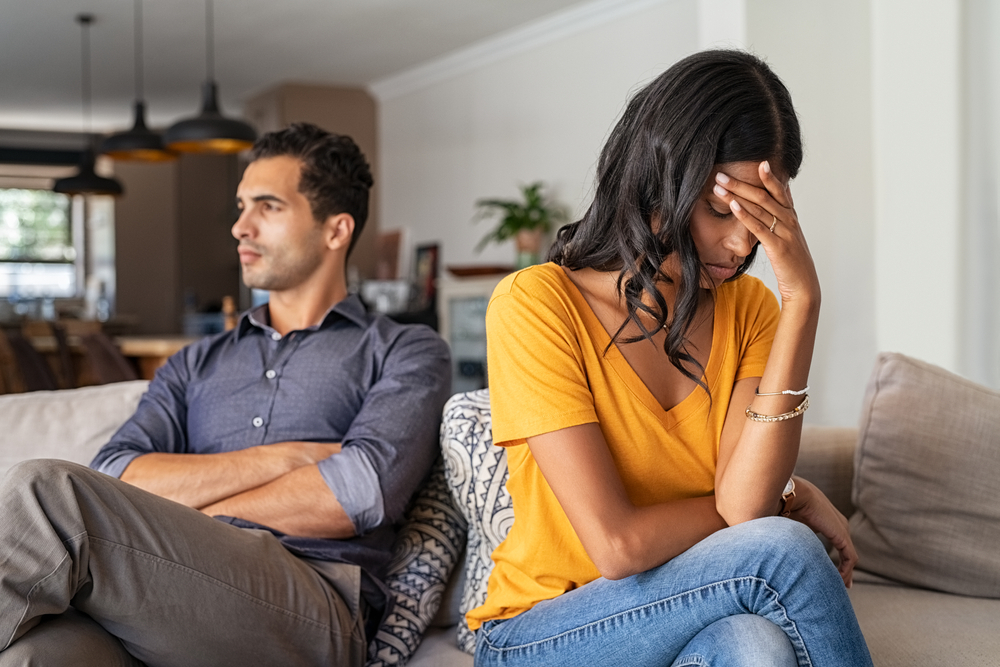 A young couple sitting on the couch while fighting and contemplating a divorce