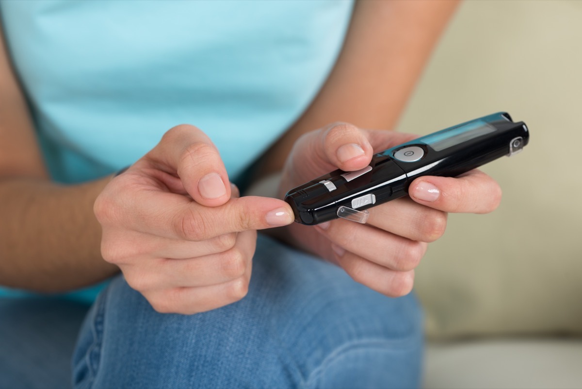 Midsection of young woman using glucometer to check blood sugar level at home