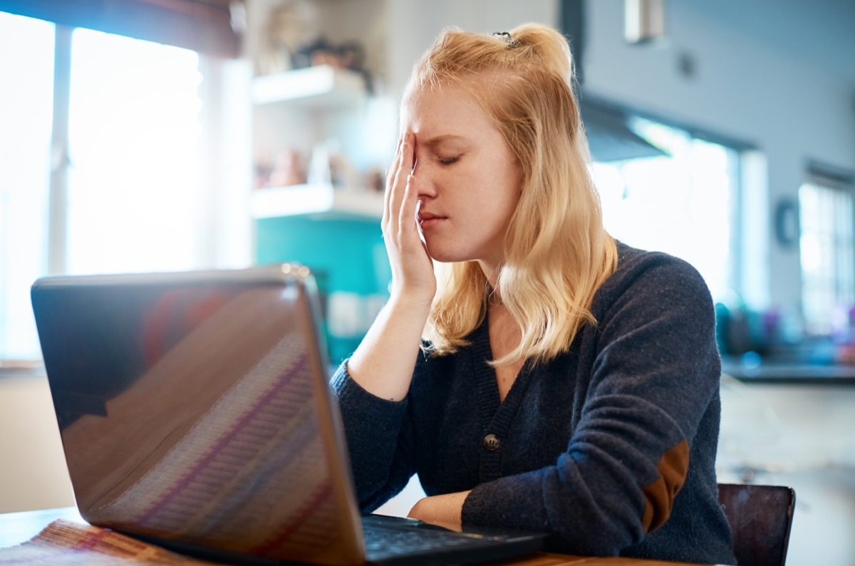 Woman using a laptop at home stops, her hand to her head.