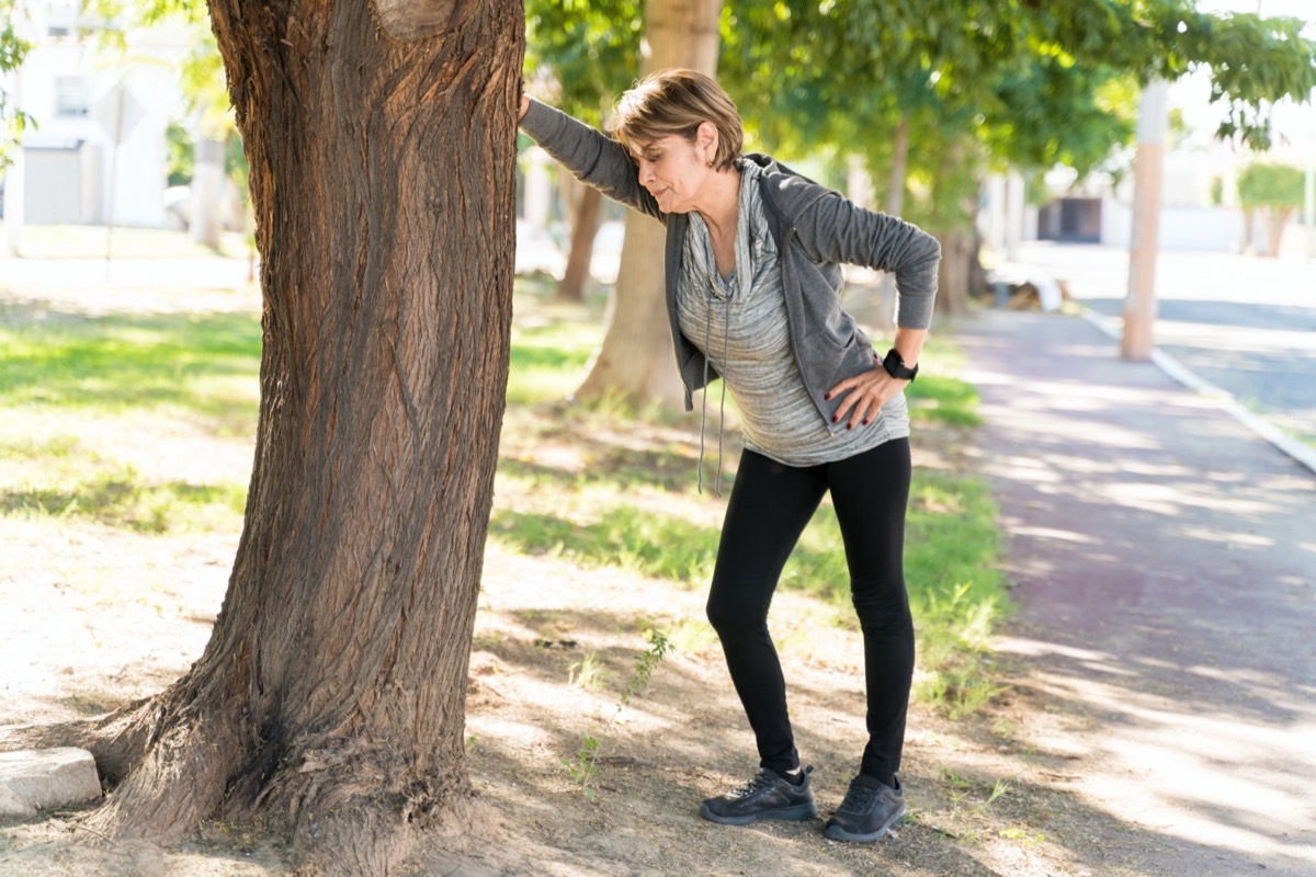 Full length of exhausted senior woman taking a break while leaning on tree in city