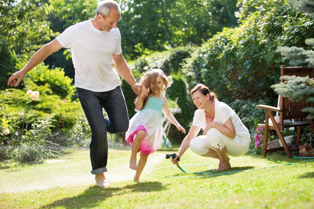 Grandpa running with granddaughter while grandmother waters the grass