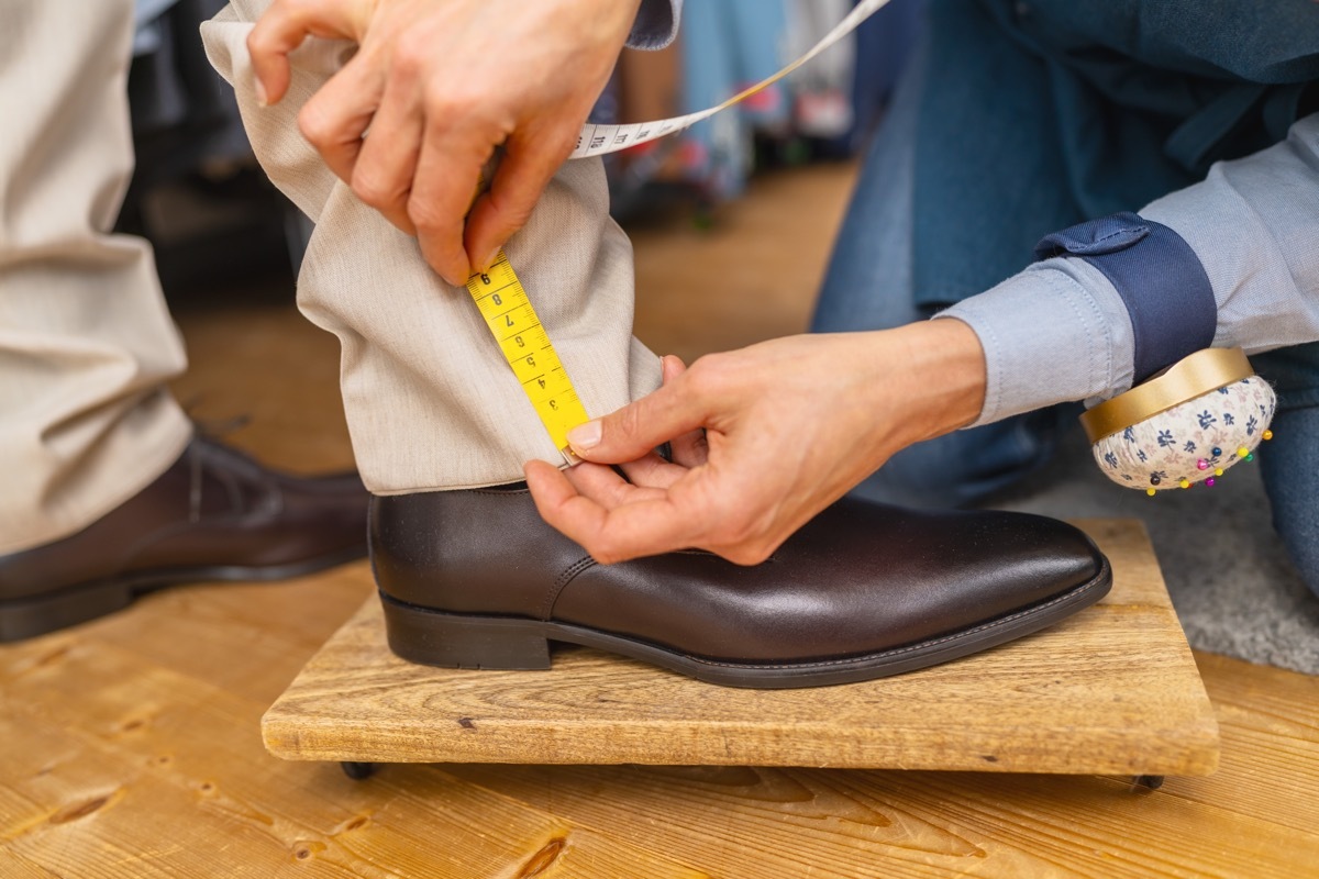 Measuring trouser length with tape on man's ankle above brown shoe