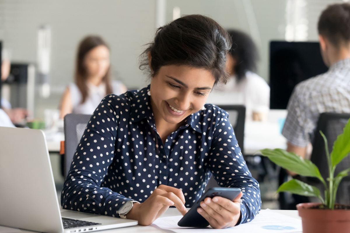 young indian woman looking at phone while at desk at work