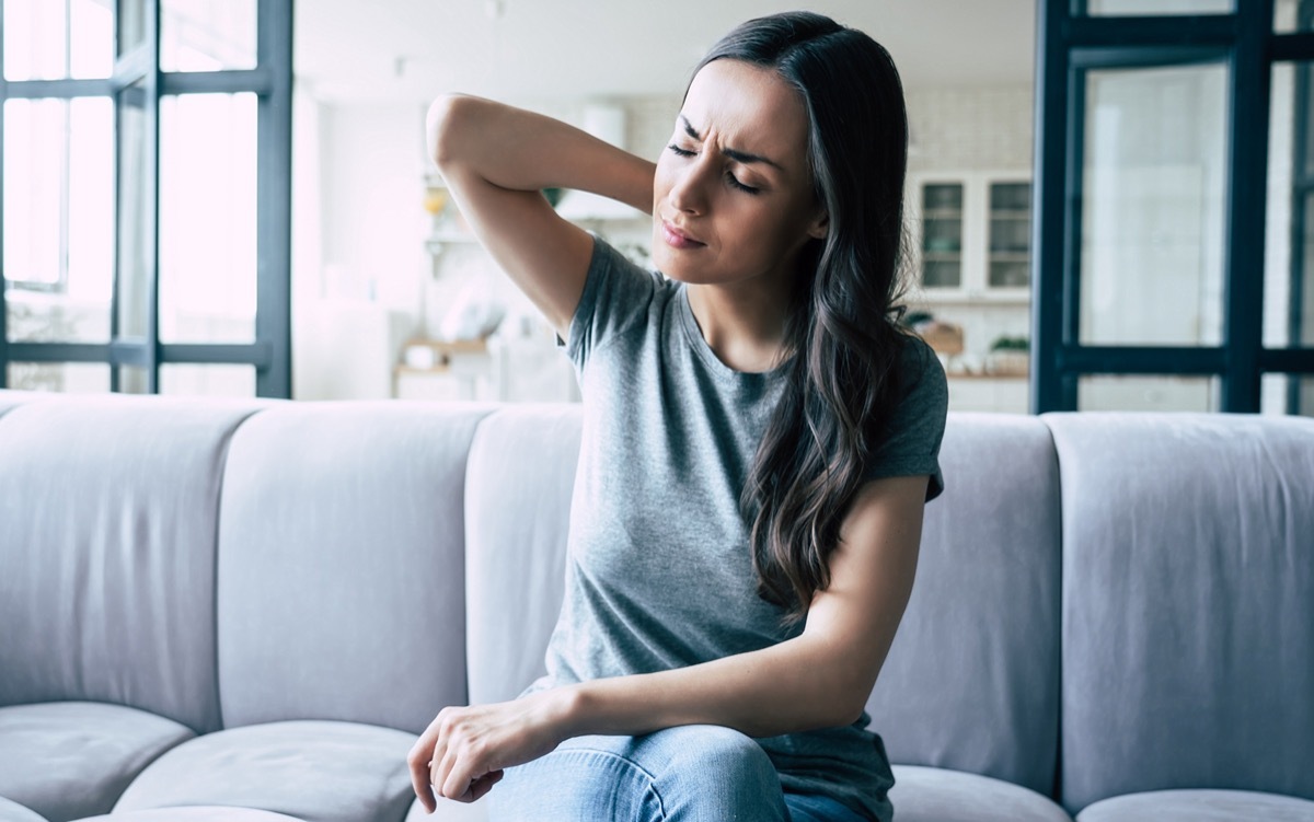 Woman in pain touching her back while sitting on the couch.