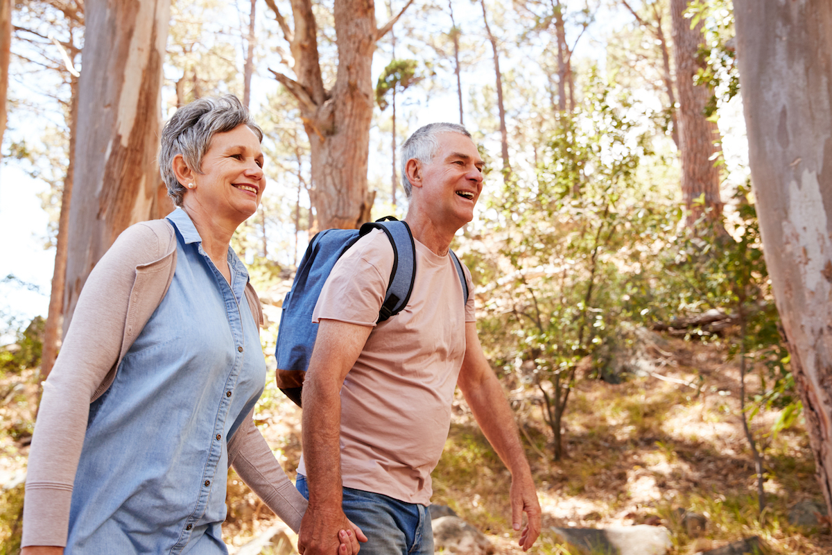 A mature couple holding hands and hiking in a forest