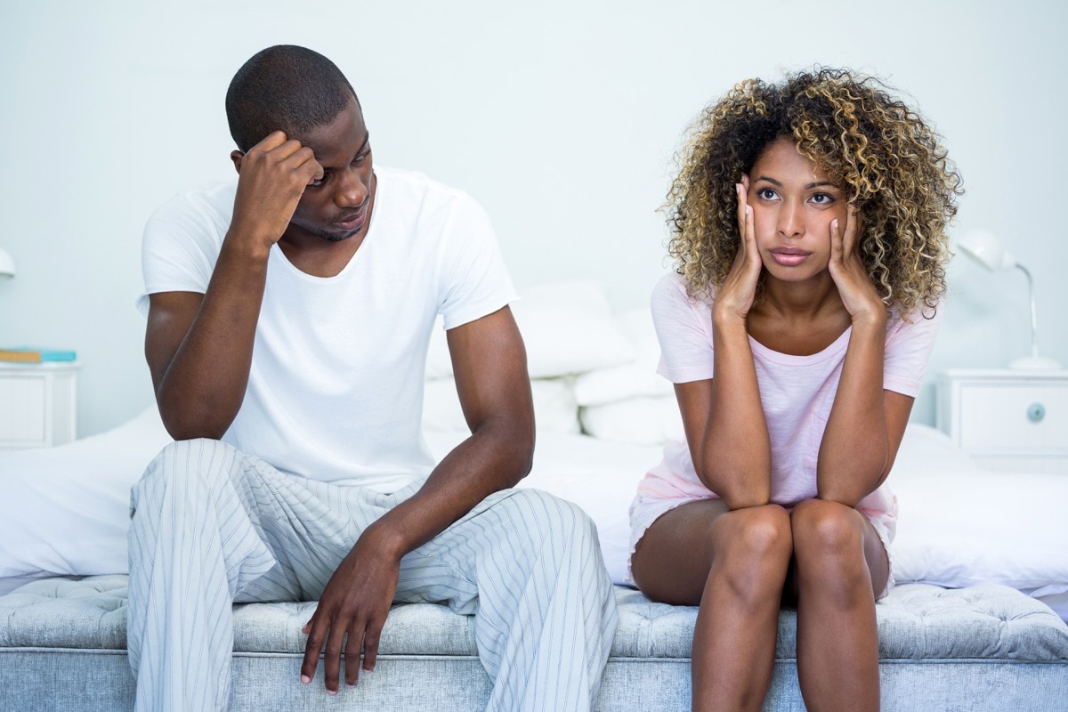 couple sitting on edge of bed looking distant and unhappy