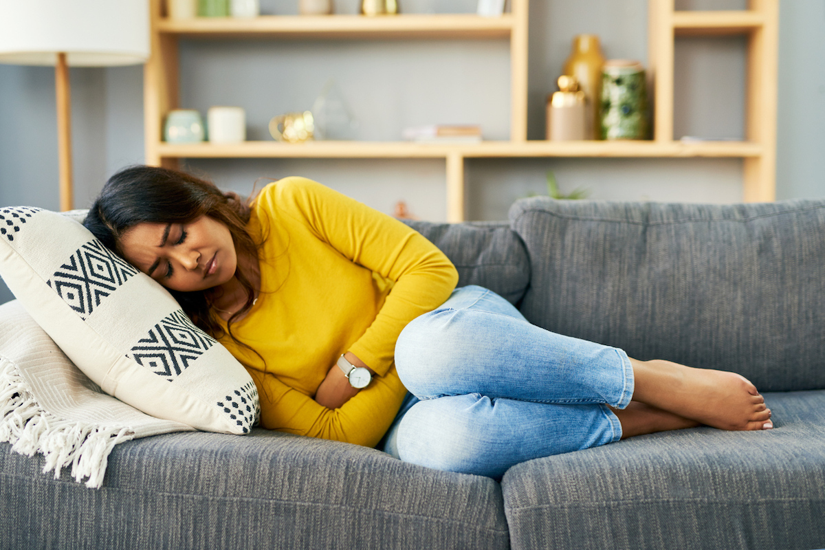 young woman suffering from stomach cramps at home on couch