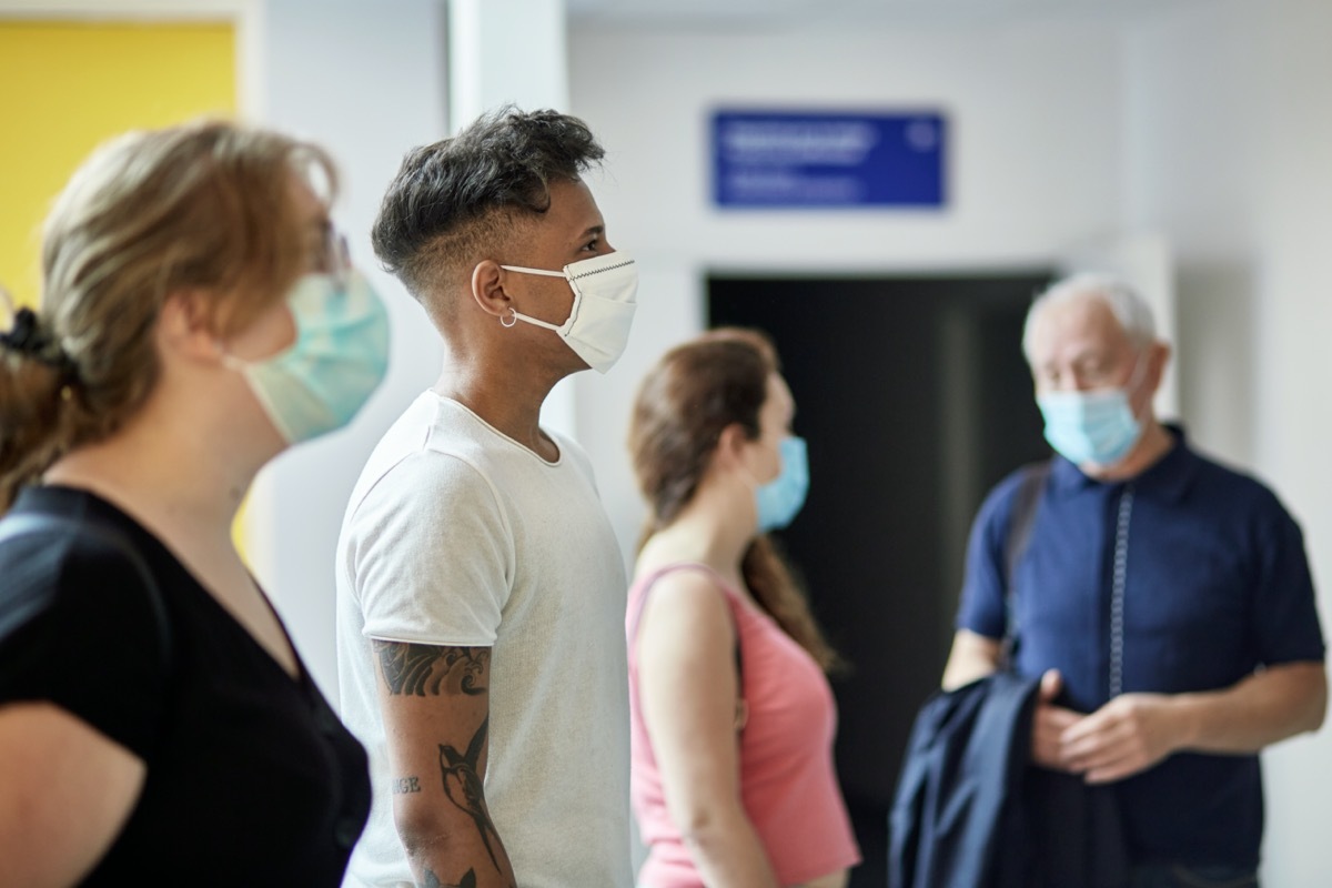 people in teens, 20s, 30s, and 60s wearing protective masks and following social distancing requirement as they stand and wait.