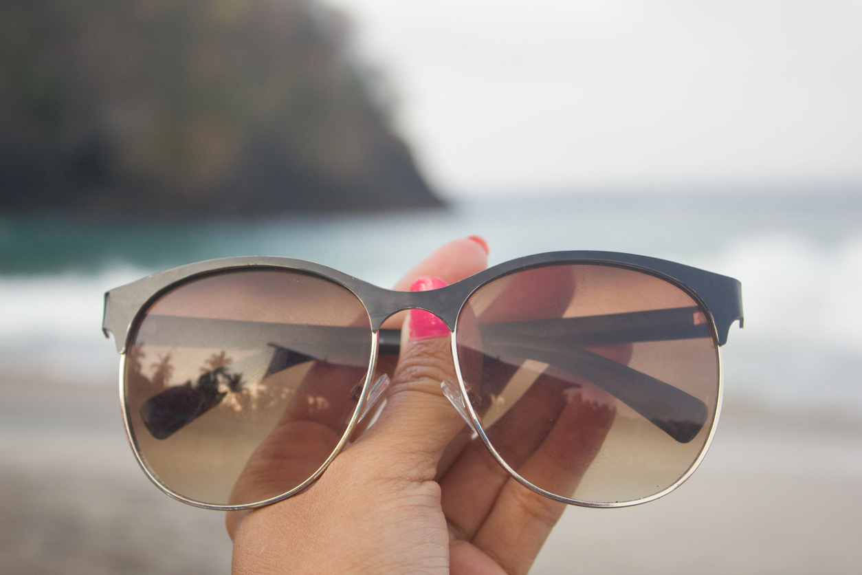 Hand holding up sunglasses with brown lenses on a beach