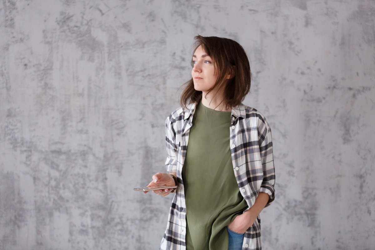 woman holding phone looking out window