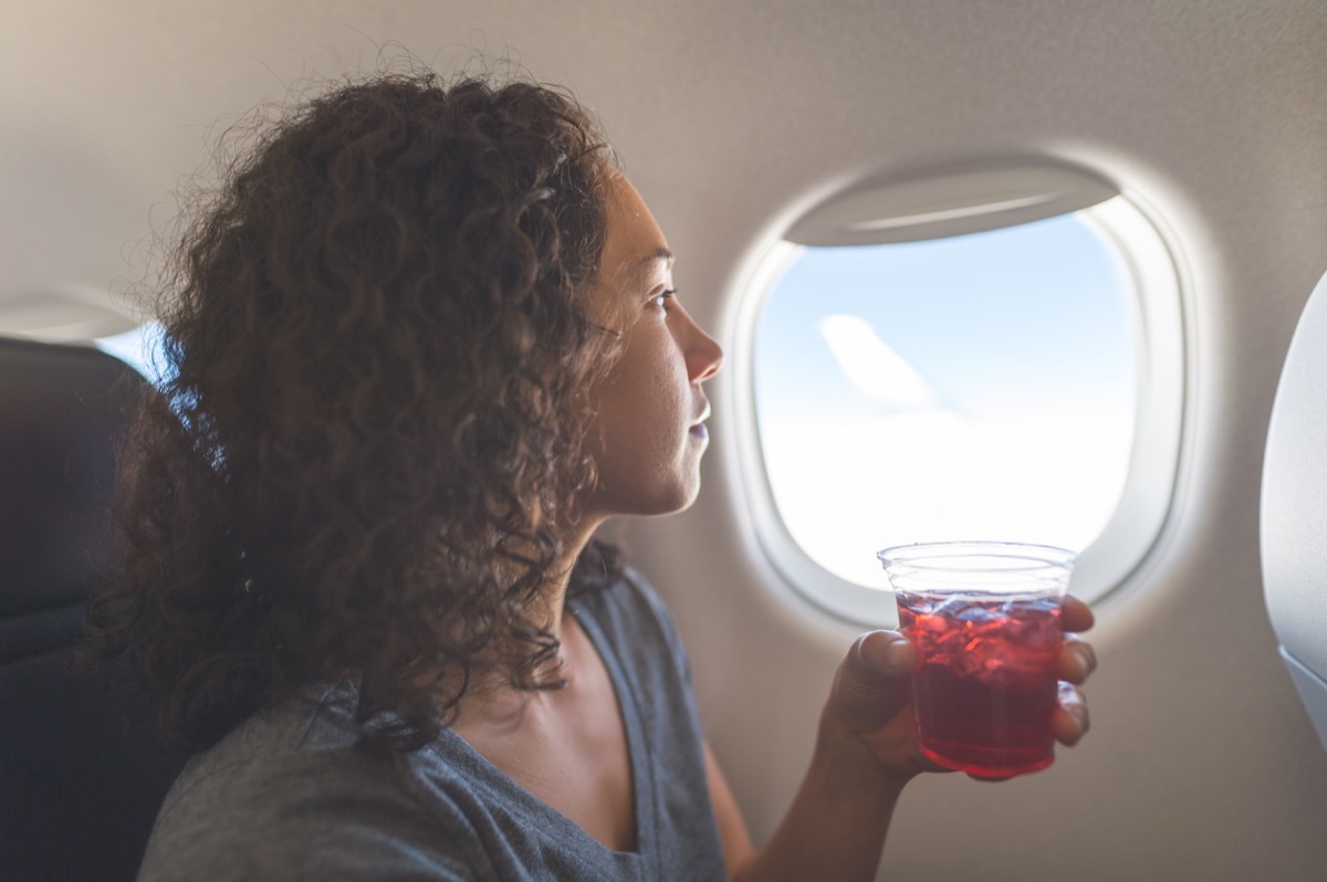 woman peacefully looks out an aircraft's window. She is sitting and holding a drink in her left hand.