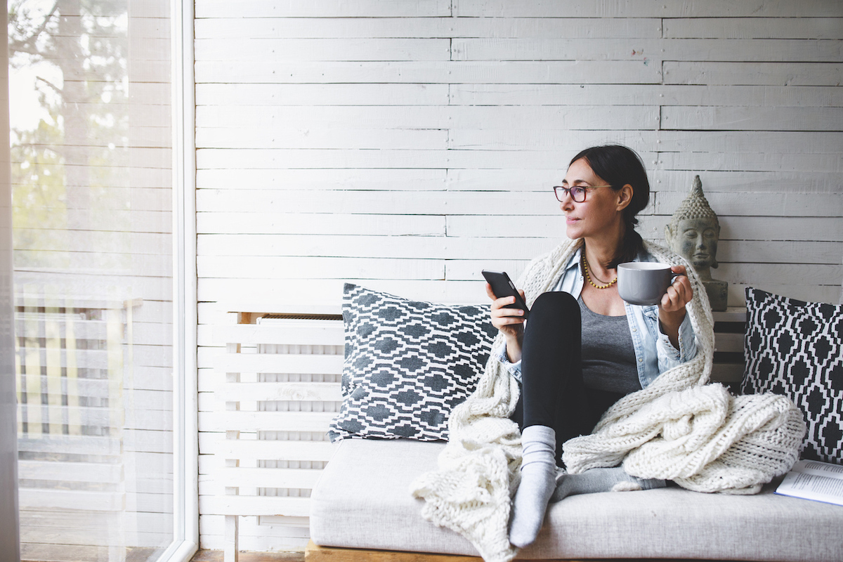 Middle-aged woman siting comfortable and enjoys tea on couch during winter