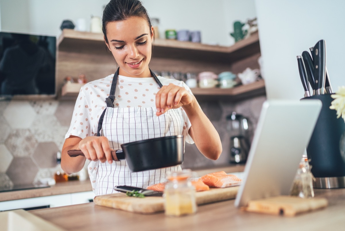 Young woman using digital tablet while cooking salmon filet in kitchen