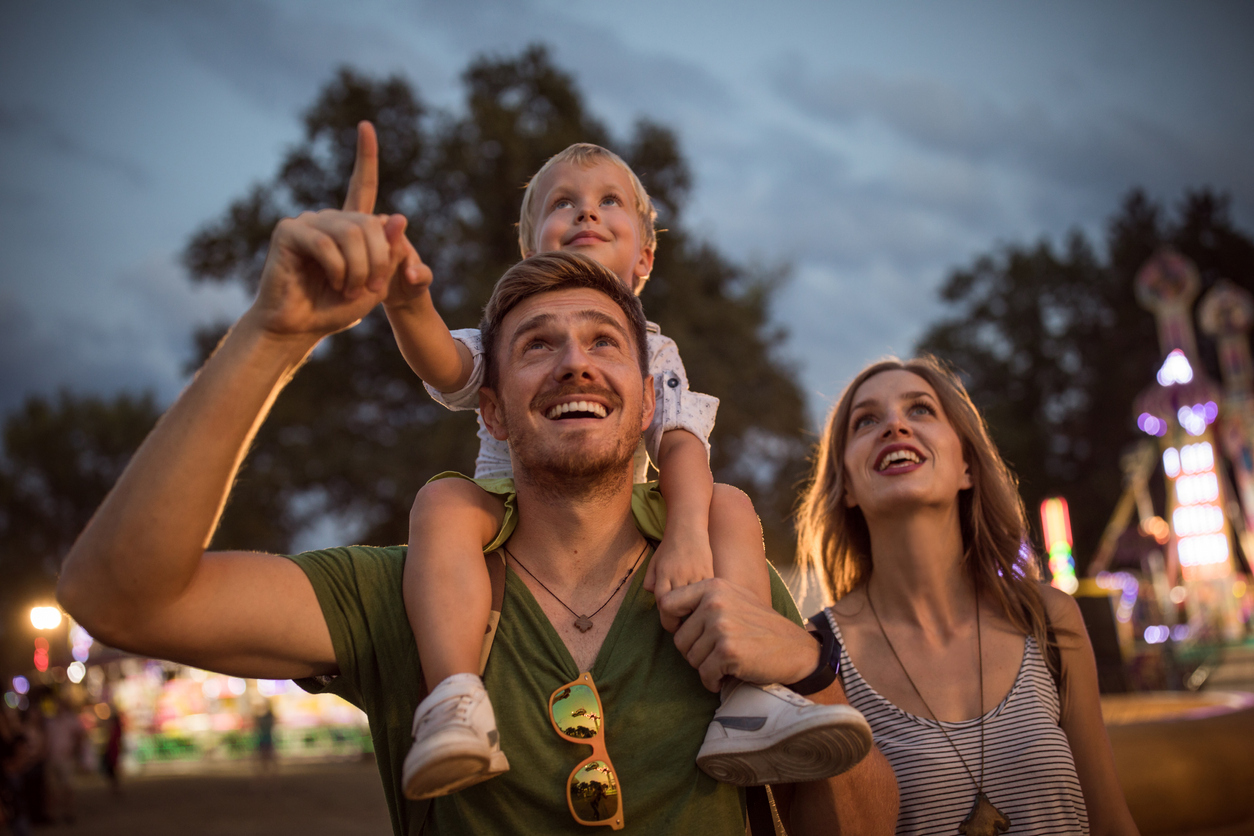 Family with one child outdoors on summer festival. Father carrying son on shoulders, they enjoy in festival entertaining