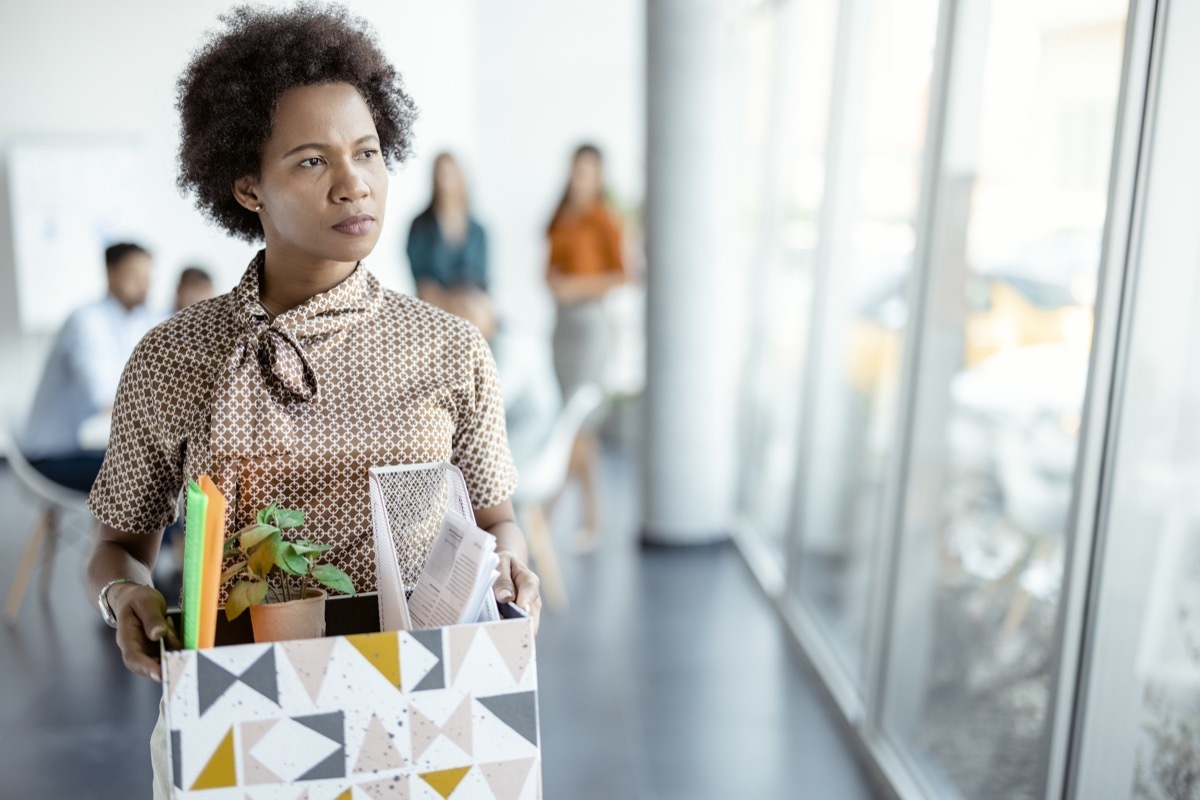 woman getting fired from work. Female walks through the office, carrying box with personal belongings. Business, firing and job loss concept