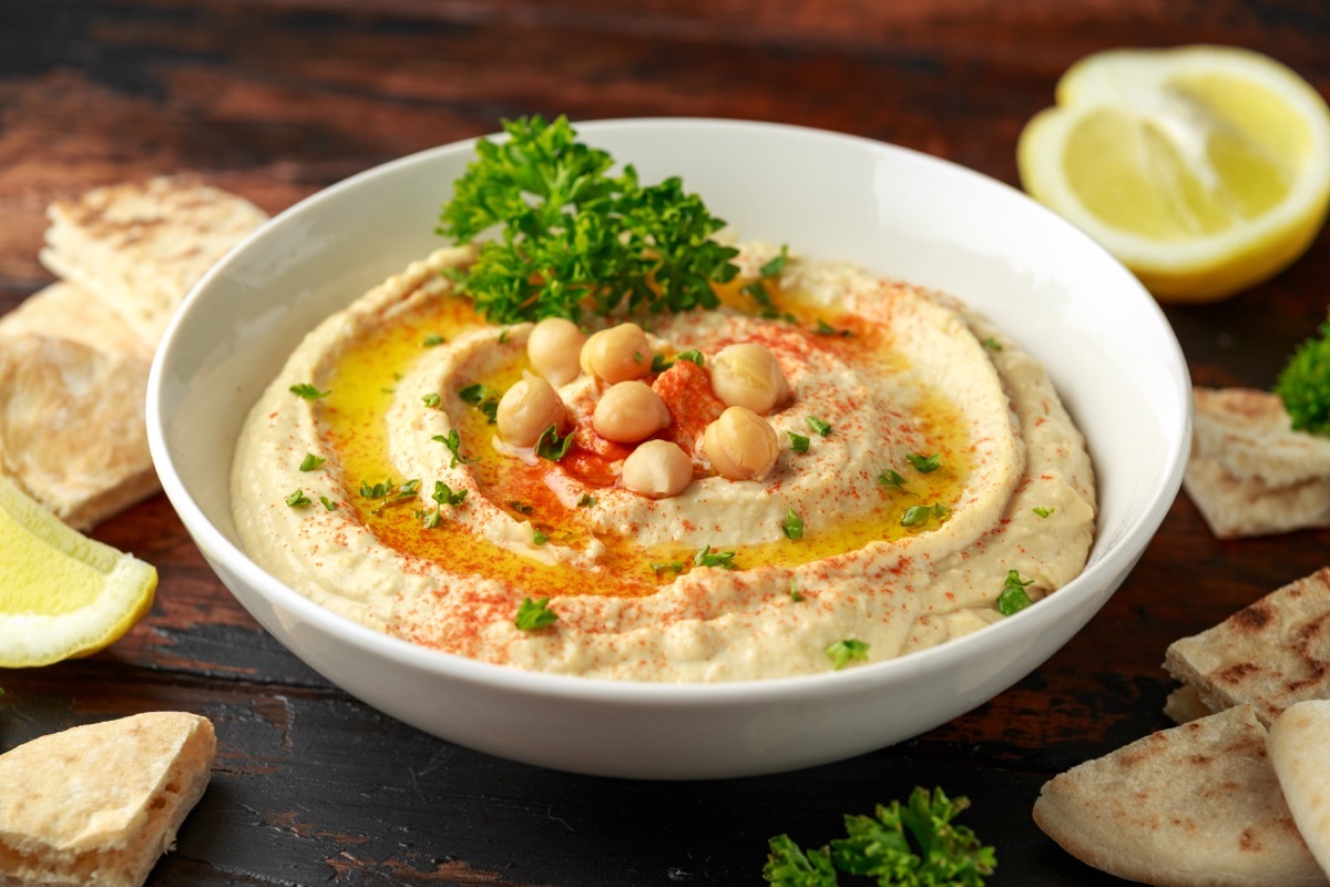 hummus in white bowl next to lemons and pita