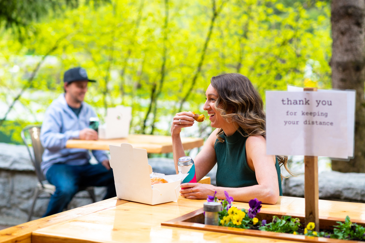 A young woman eating at a restaurant while socially distanced from other customers