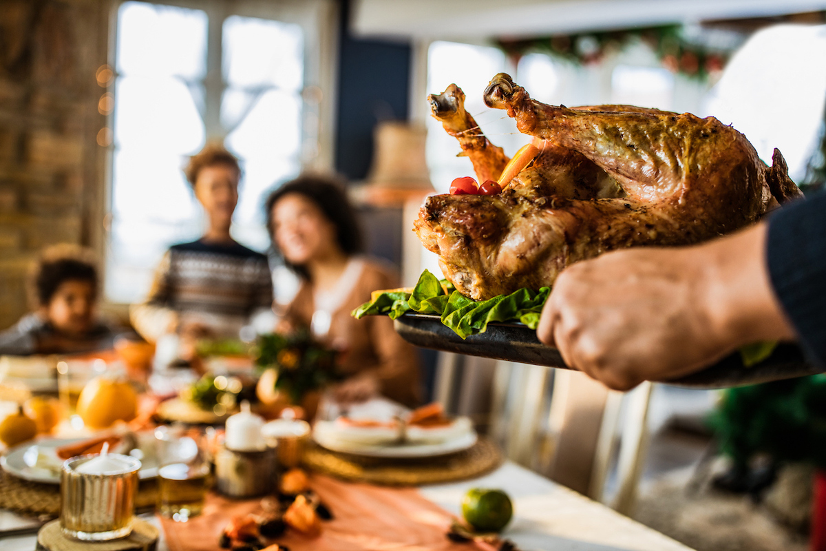 Close up of unrecognizable person carrying Thanksgiving turkey in dining room.