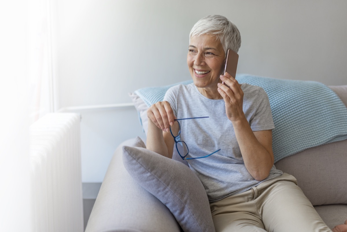 Senior woman talking on her mobile phone. Senior woman has a happy conversation at cellphone. Smiling senior woman using phone sitting on couch at home.