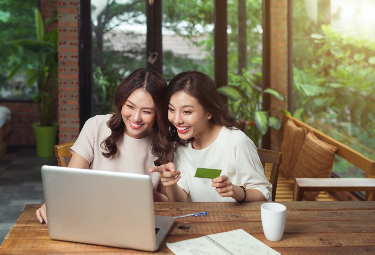 two Asian-Americans looking at pointing at something on a laptop and one of the girls holding a green card