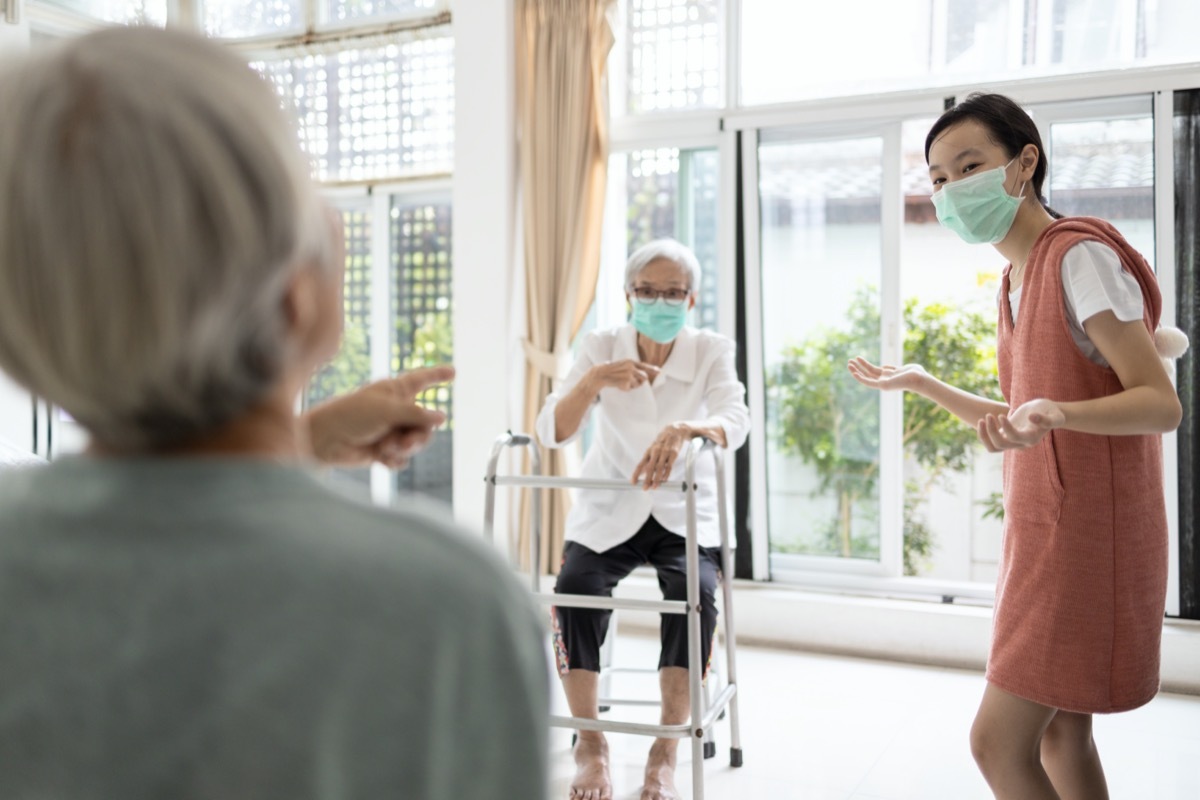 Family of elderly,senior woman,child girl are talking by maintain distancing,prevent infection of flu,Coronavirus,pandemic of Covid-19,people with prevention mask,maintain social distance for safety