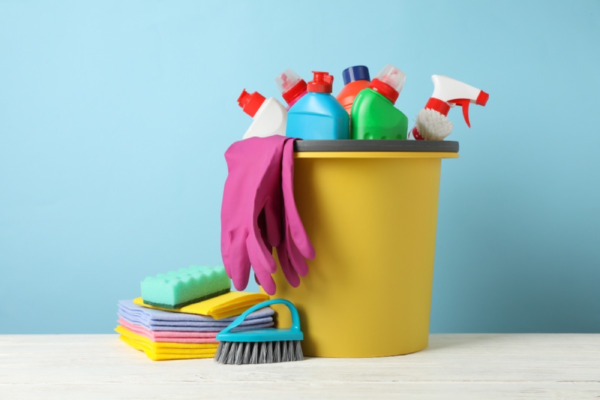 colorful cleaning supplies in yellow bucket on blue background